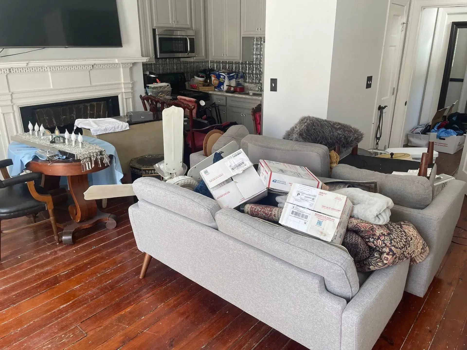 Cluttered living room with couch, boxes, furniture, and fireplace. Hardwood floors.