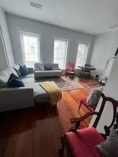 Living room with gray sectional sofa, hardwood floors, three windows, and a red chair.