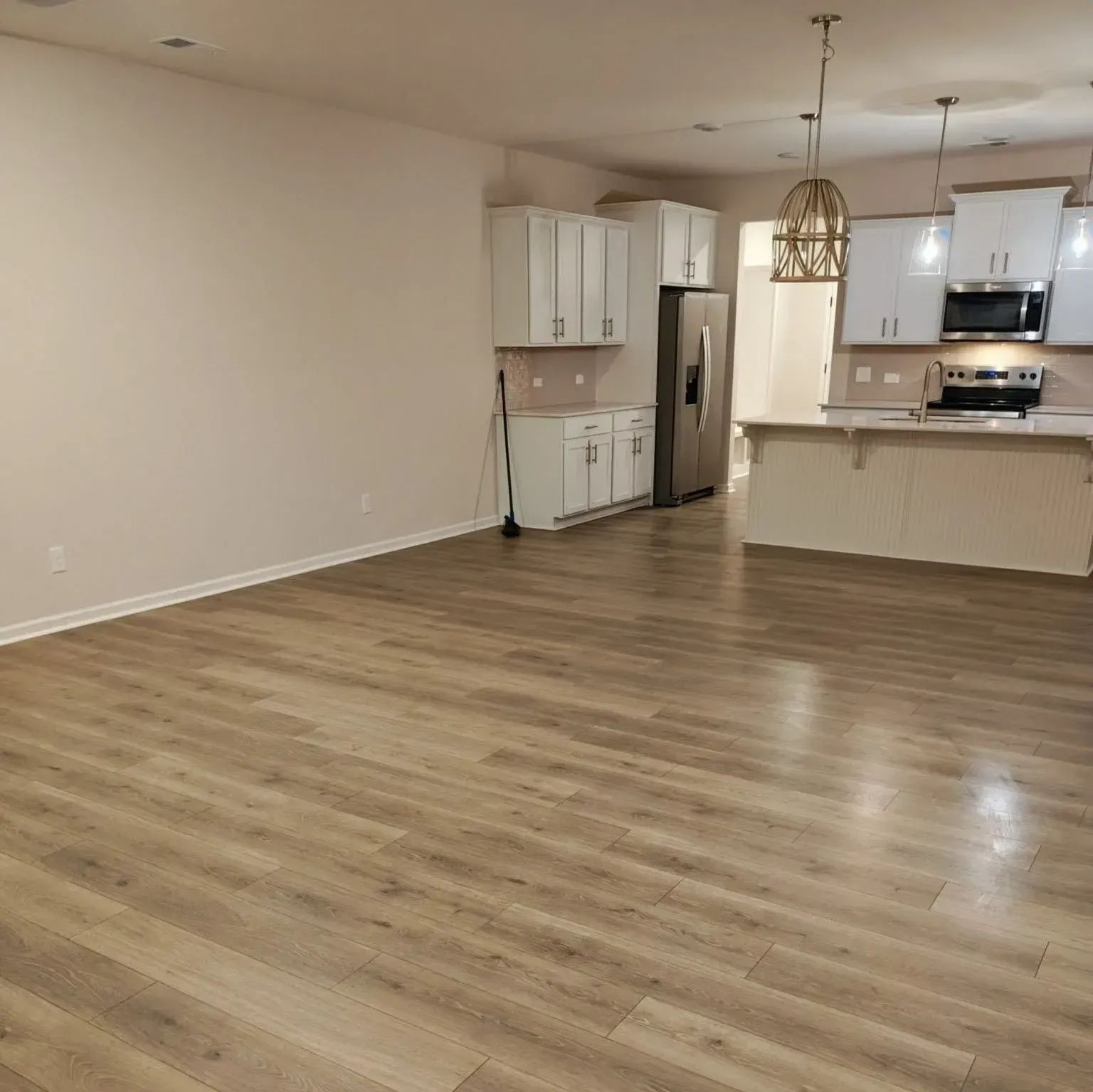 Empty open-plan kitchen and living room with light wood floors and white cabinets.