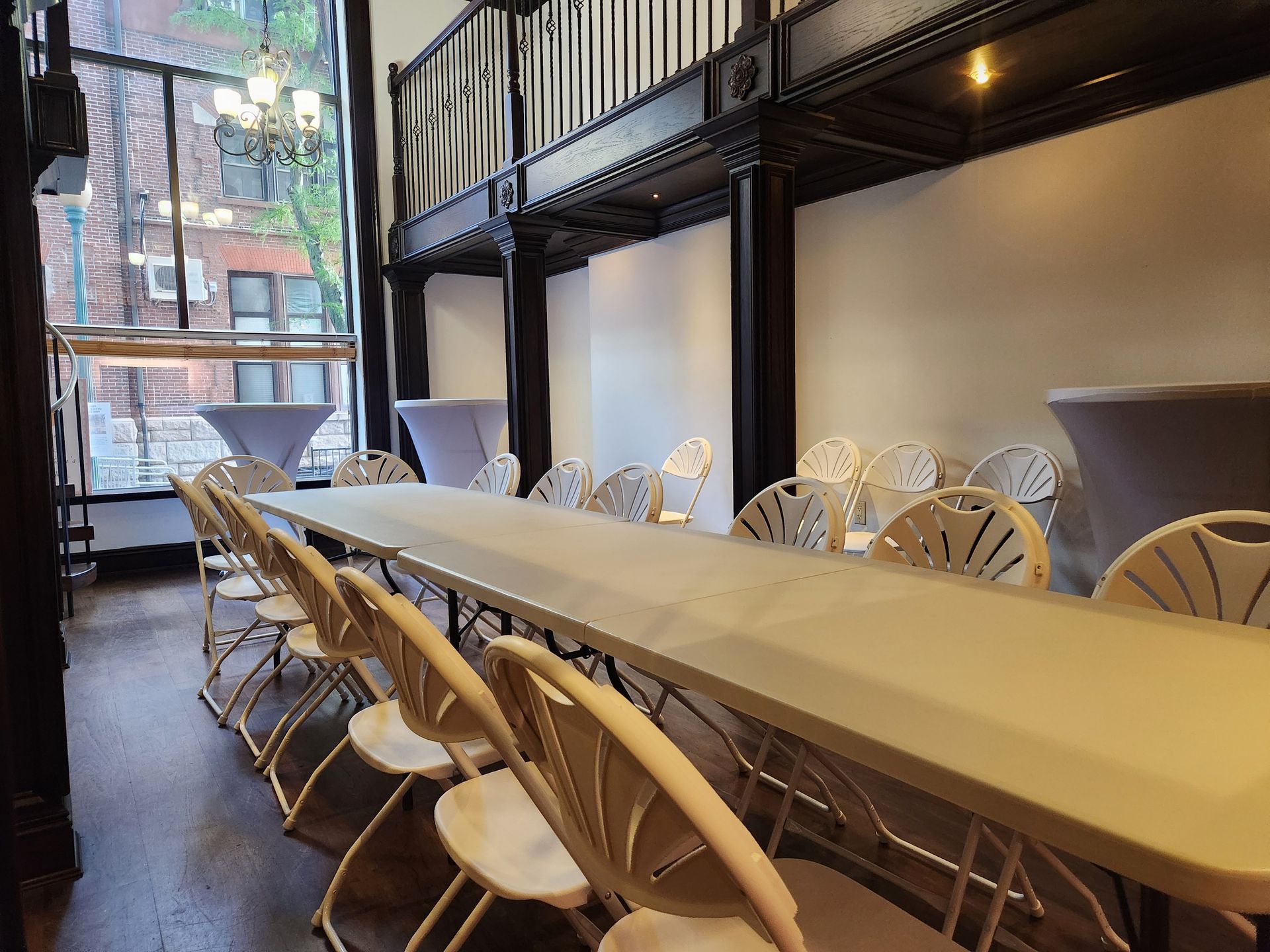 Long rectangular table with many white folding chairs in a venue with a loft area, looking out a large window.