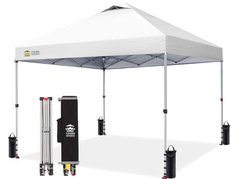 White pop-up canopy with one side wall, with its folded frame and carrying case displayed. Sandbags anchor each leg.