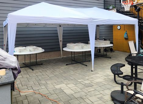 White canopy over outdoor tables set up on a patio; a few tables hold covered food items.