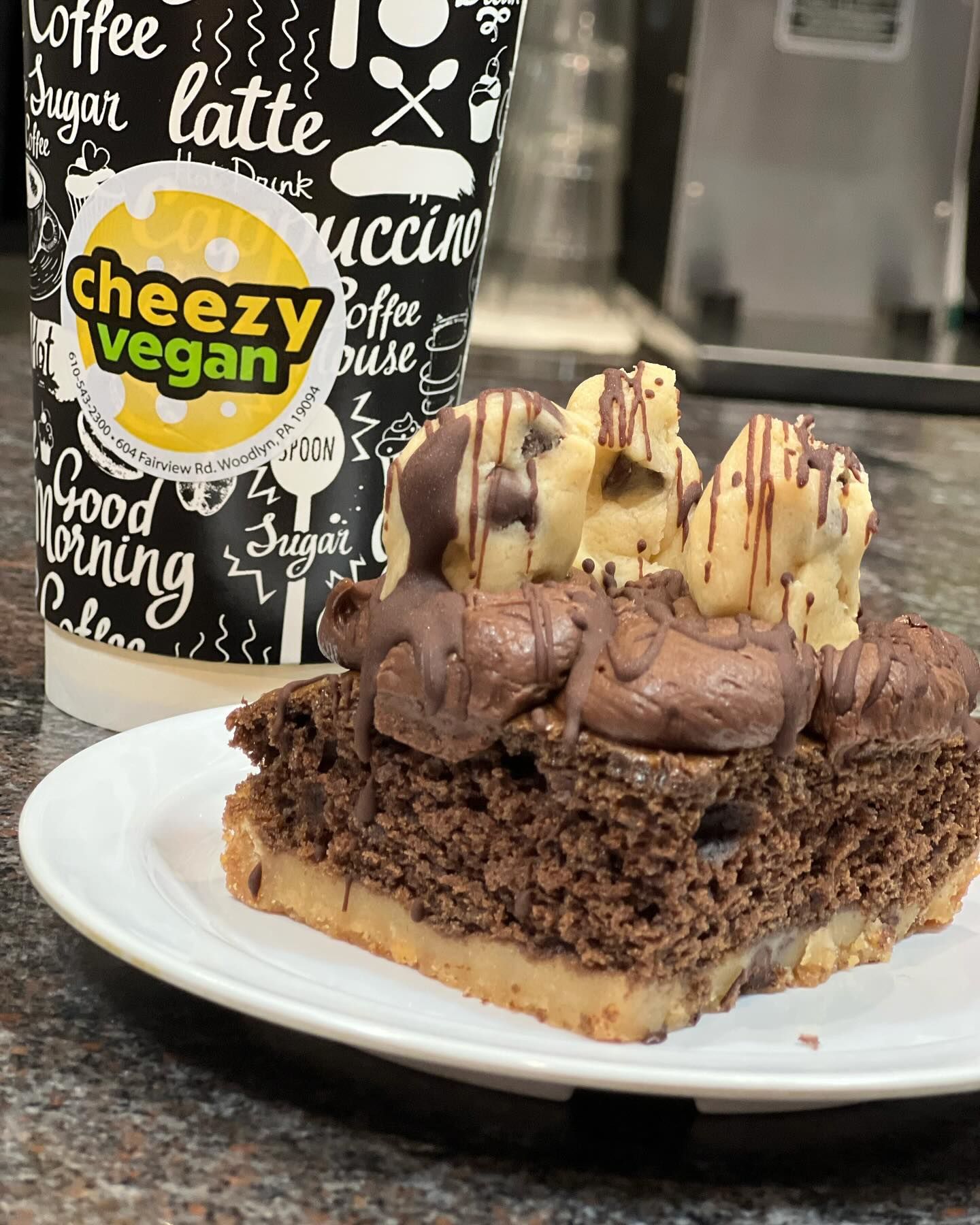 Coffee cup and chocolate cake slice on a white plate in a cafe setting.