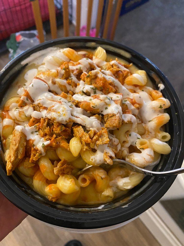 Mac and cheese with buffalo chicken and drizzle of white sauce in a black bowl.