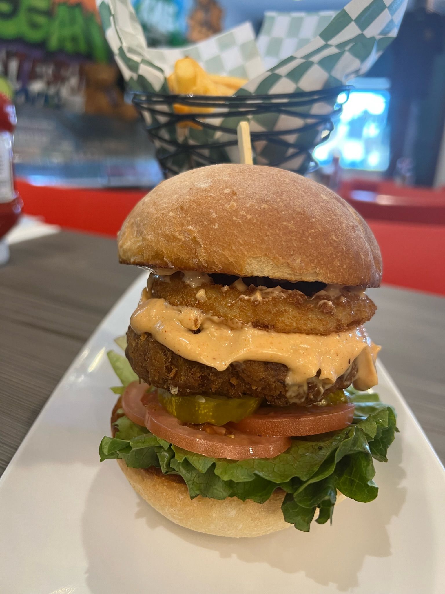 Triple-decker burger with lettuce, tomato, pickles, and sauce on a white plate with a basket liner in the background