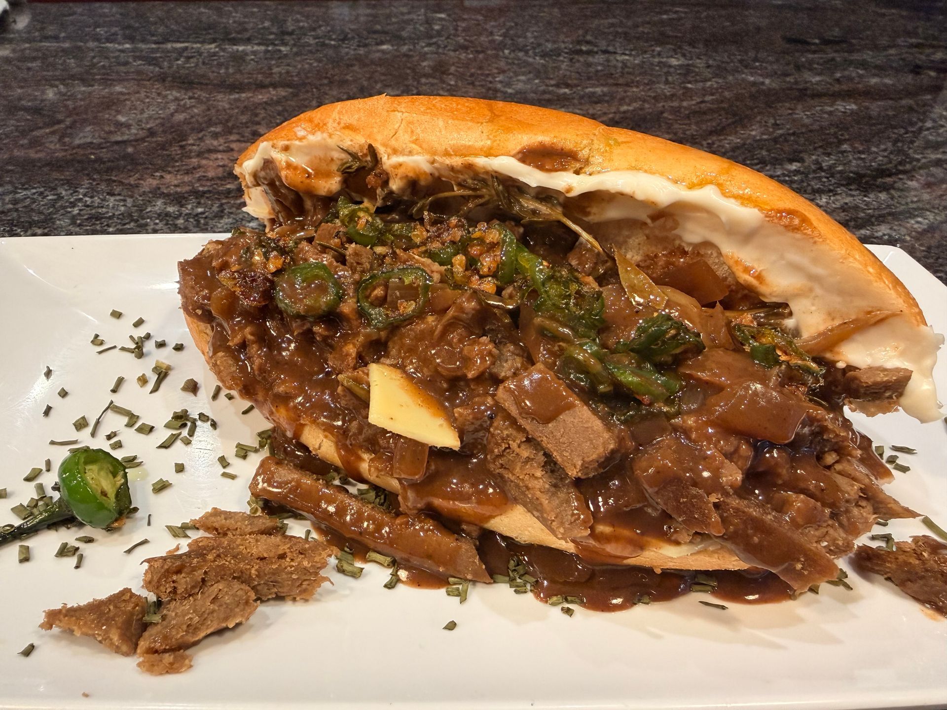 Loaded sandwich with meat and greens on a plate, with garnish scattered beside it.