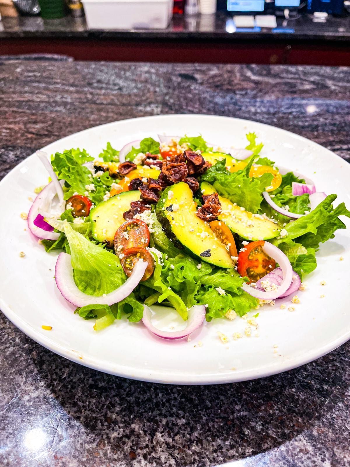 A fresh salad with lettuce, avocado slices, red onion, and cherry tomatoes on a white plate set on a granite countertop.