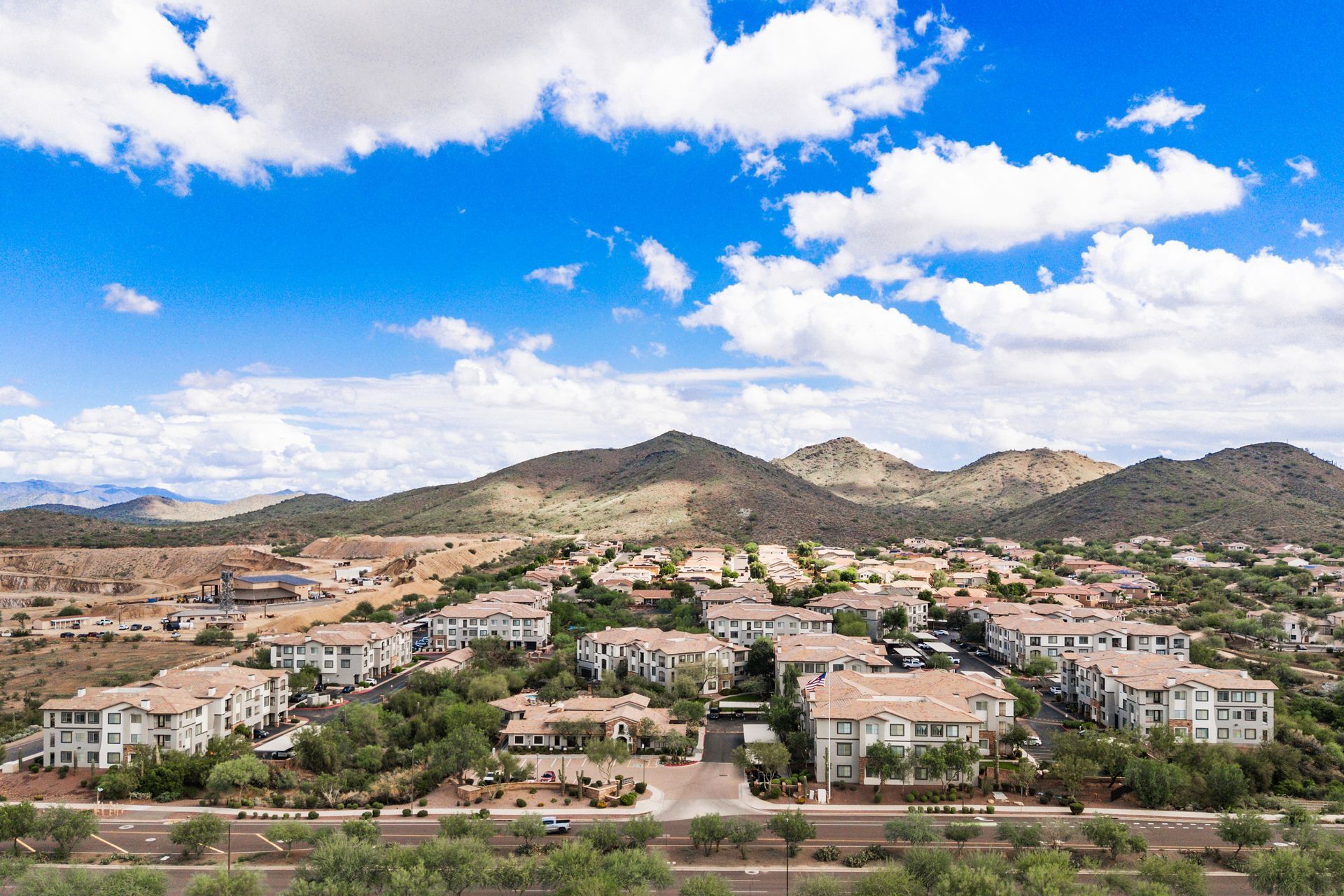 Suburban homes at the base of dry mountains under a bright blue sky with scattered clouds