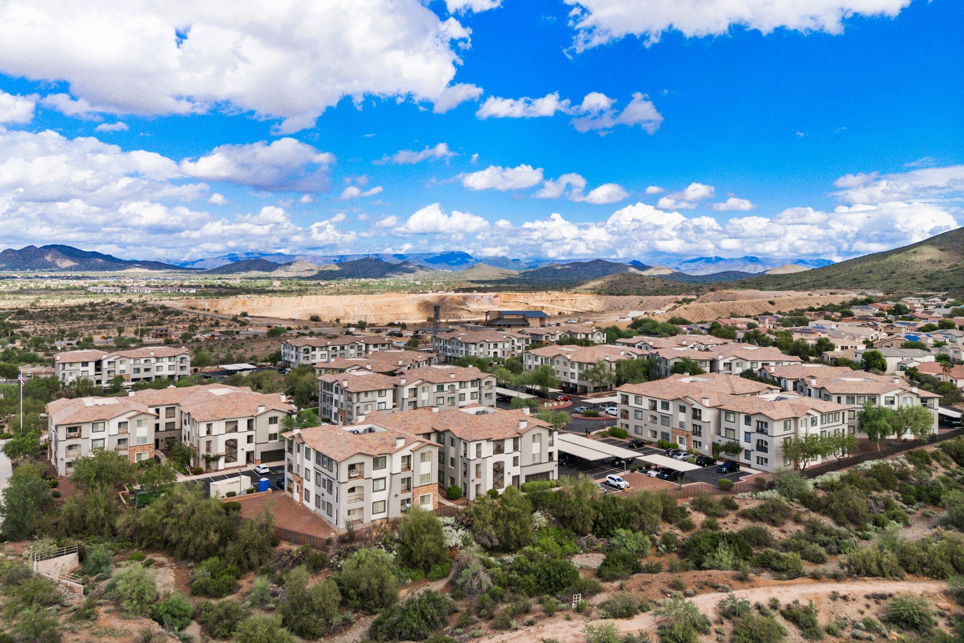 Aerial view of a suburban apartment complex with beige buildings under a bright blue, cloudy sky.