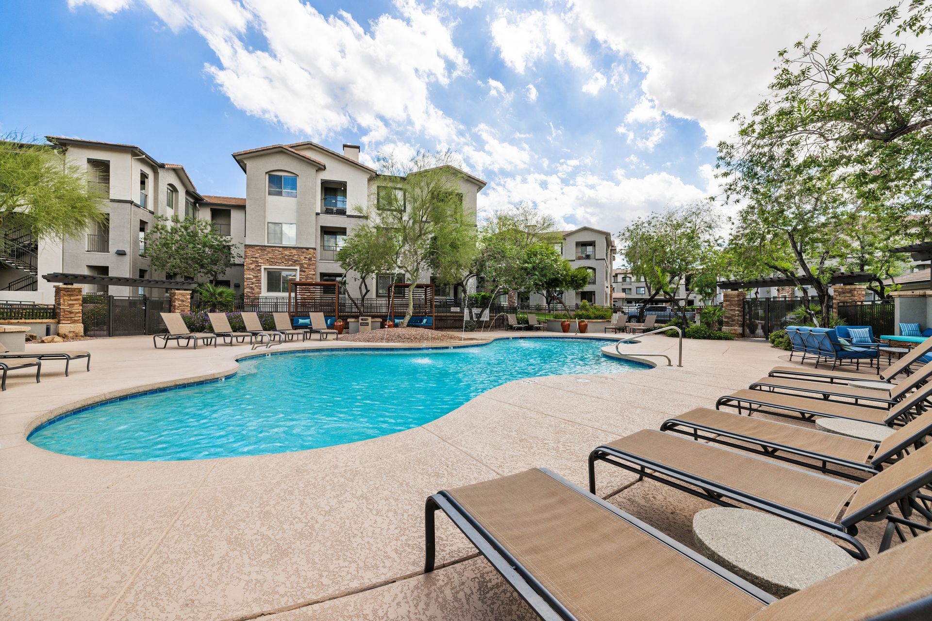 Apartment complex pool with lounge chairs and blue umbrellas on a sunny day