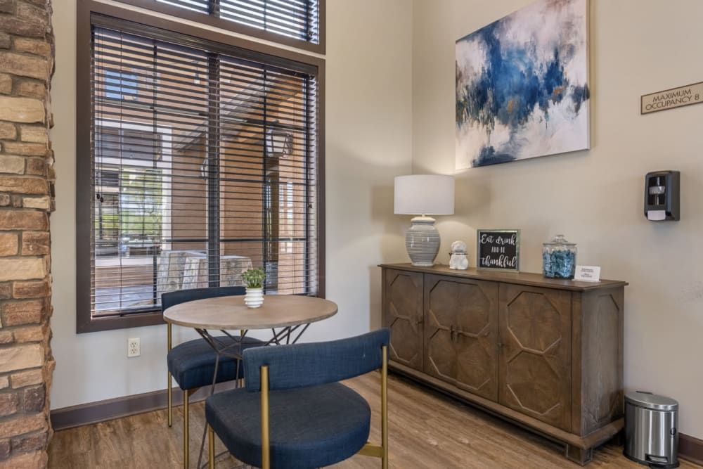 Cozy office nook with round table, blue chairs, window blinds, sideboard, lamp, and abstract wall art