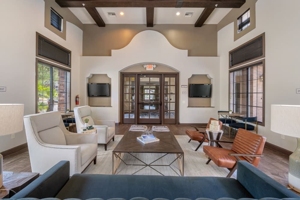 Apartment clubhouse with tall ceilings, sofas, armchairs, and glass doors in a bright neutral interior