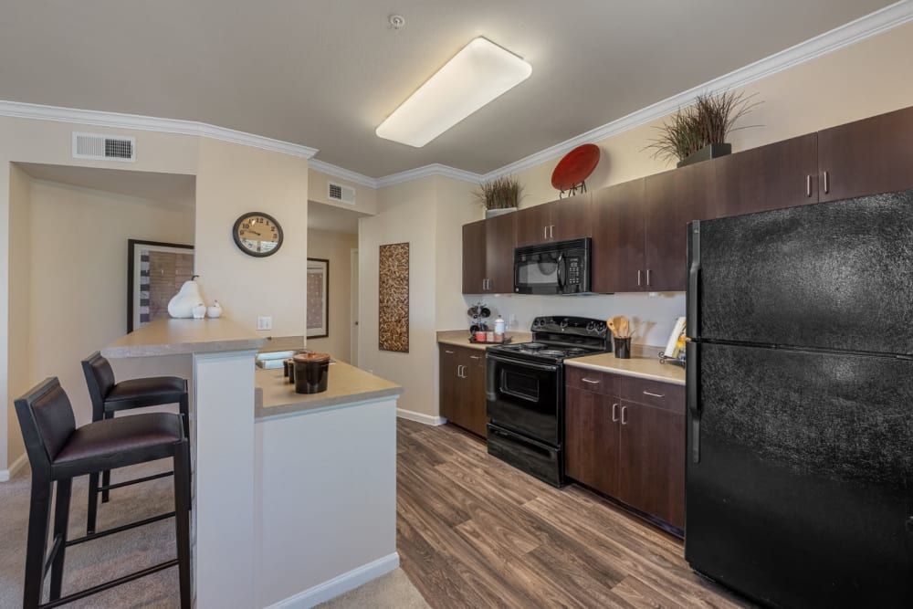 Modern kitchen with dark cabinets, black appliances, wood-look flooring, and a white island