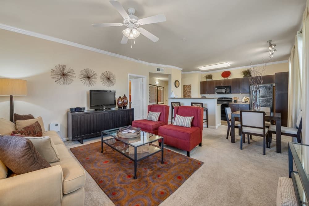 Spacious apartment living room with beige sofa, red chairs, TV, fireplace, and dining area in the background