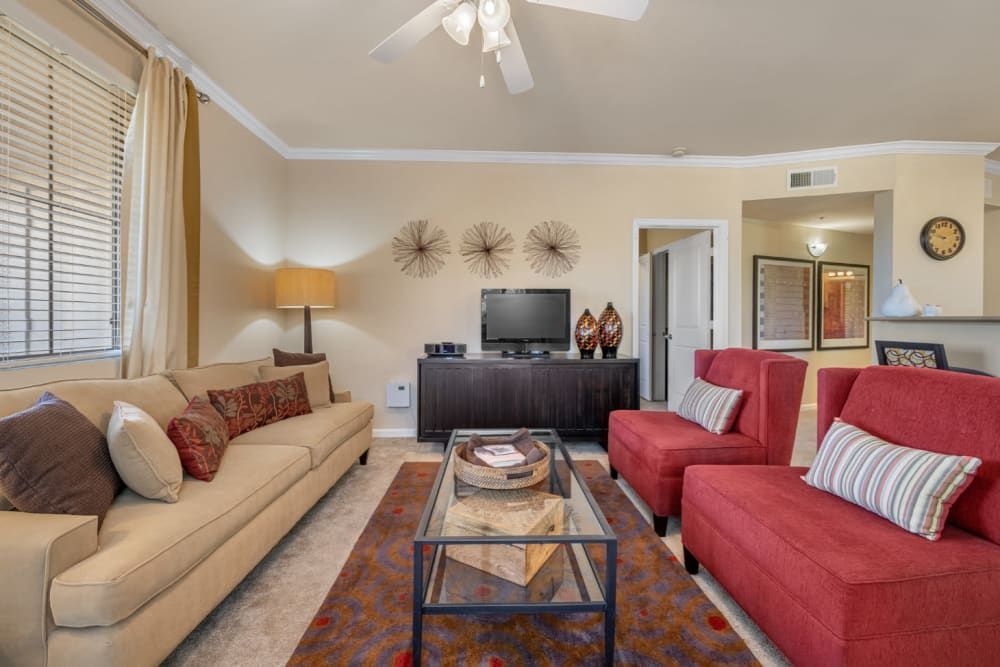 Apartment living room with beige and red sofas, coffee table, TV console, lamp, and wall art