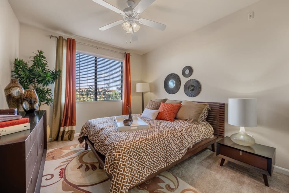 Bedroom with patterned bedspread, large window, ceiling fan, and warm beige decor