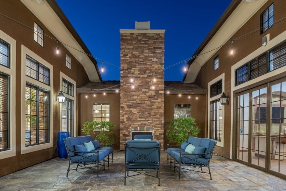 Brick courtyard patio with blue chairs, potted plants, and glass doors between two buildings at dusk