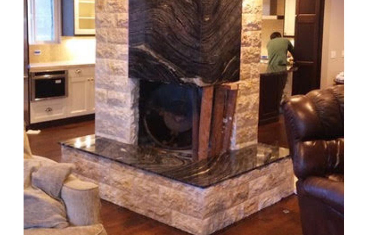 Stone fireplace with dark granite, in a living room. A person is visible in the background.