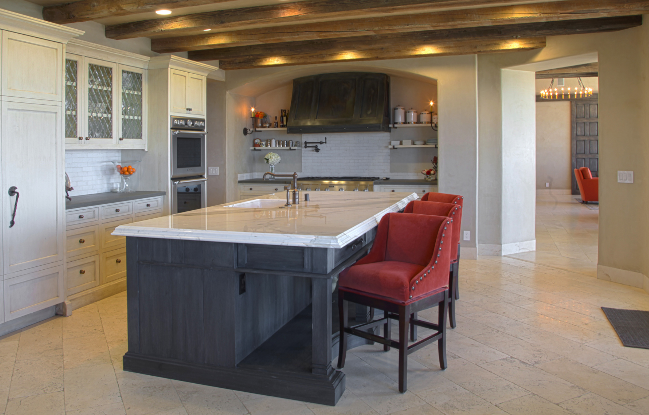 Kitchen with a large island, red bar stools, white cabinets, and wood beams.