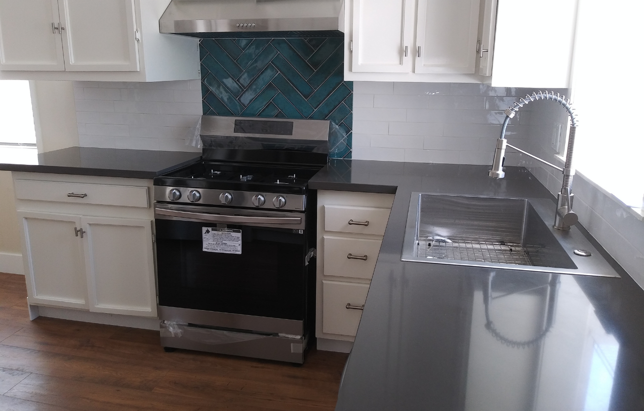 Kitchen with white cabinets, black countertops, stainless steel appliances, and teal backsplash.