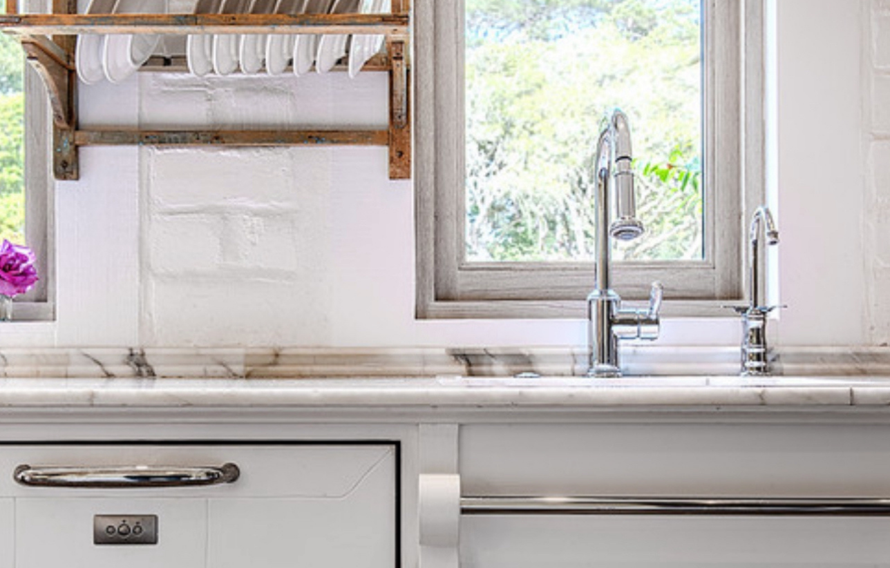 Kitchen with white cabinets, marble countertop, chrome faucet, and a window with a sunny view.