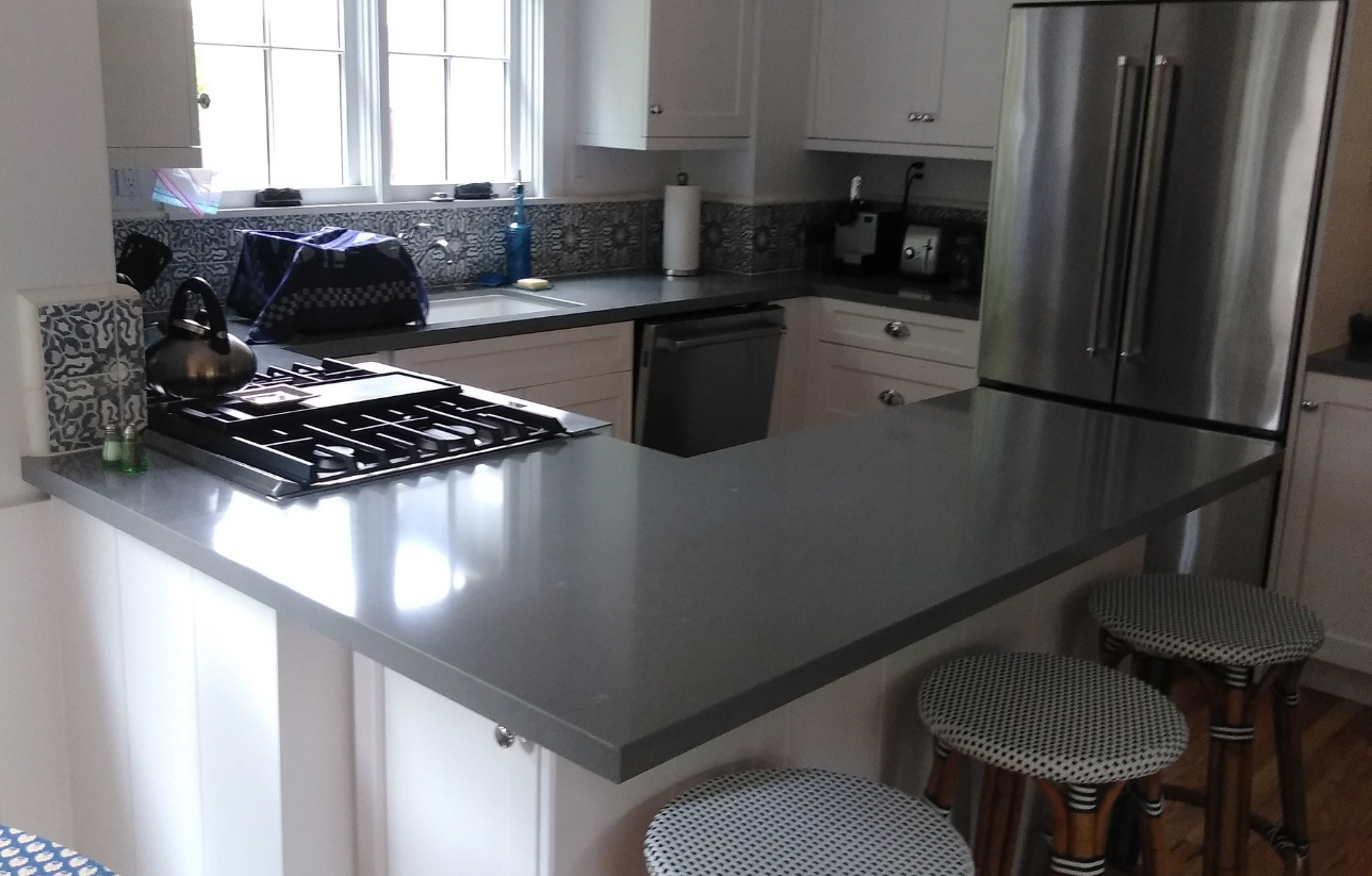 Gray countertop kitchen with white cabinets, stainless steel fridge, and two striped bar stools.