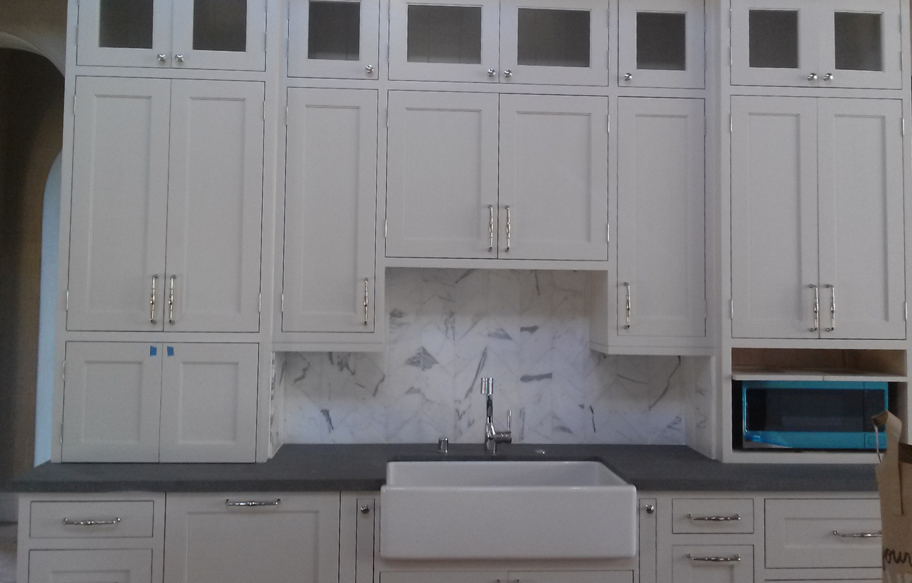 White kitchen cabinets with a farmhouse sink, gray countertop, and built-in microwave.