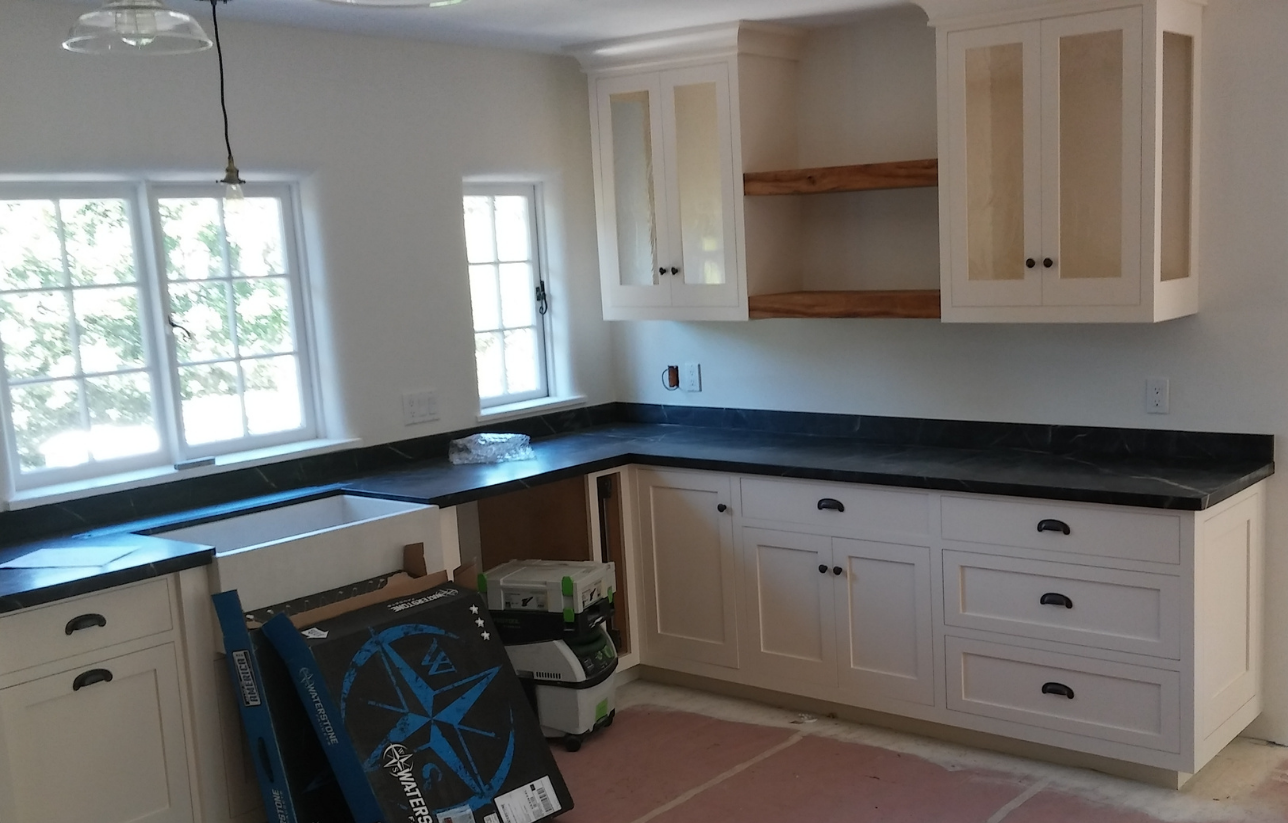 L-shaped kitchen with white cabinets, black countertops, and wood shelving under the cabinets.
