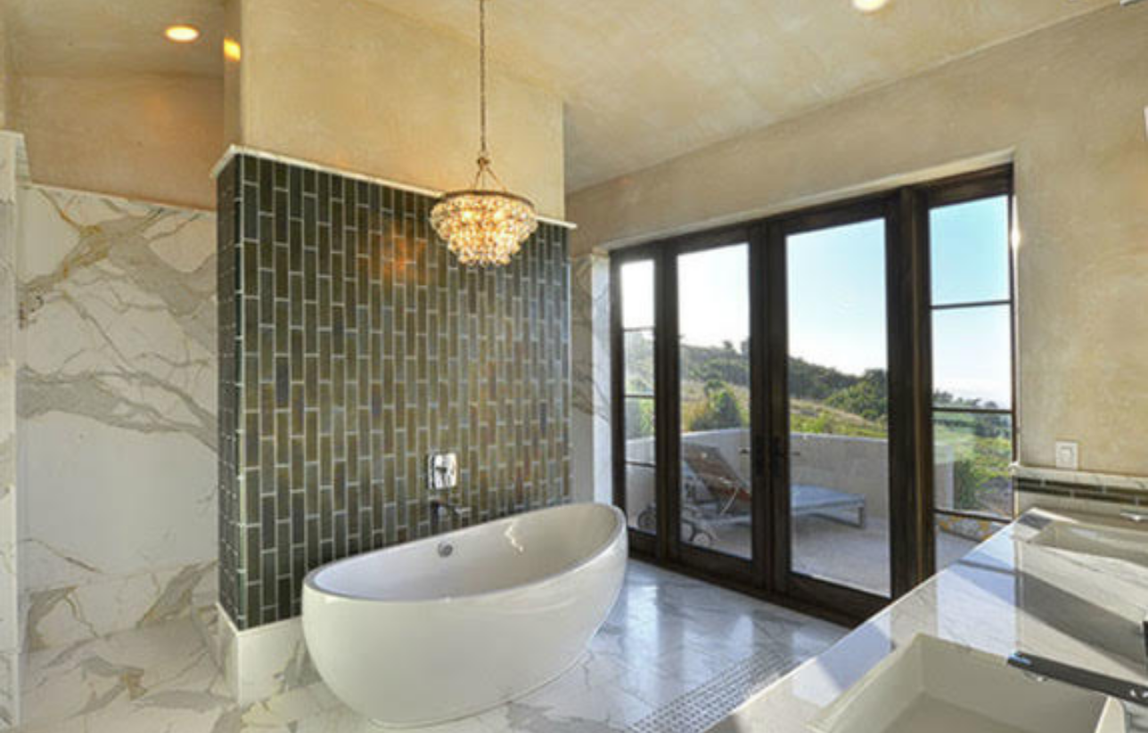 Luxurious bathroom with a white tub, green tiled wall, and large windows overlooking a view.