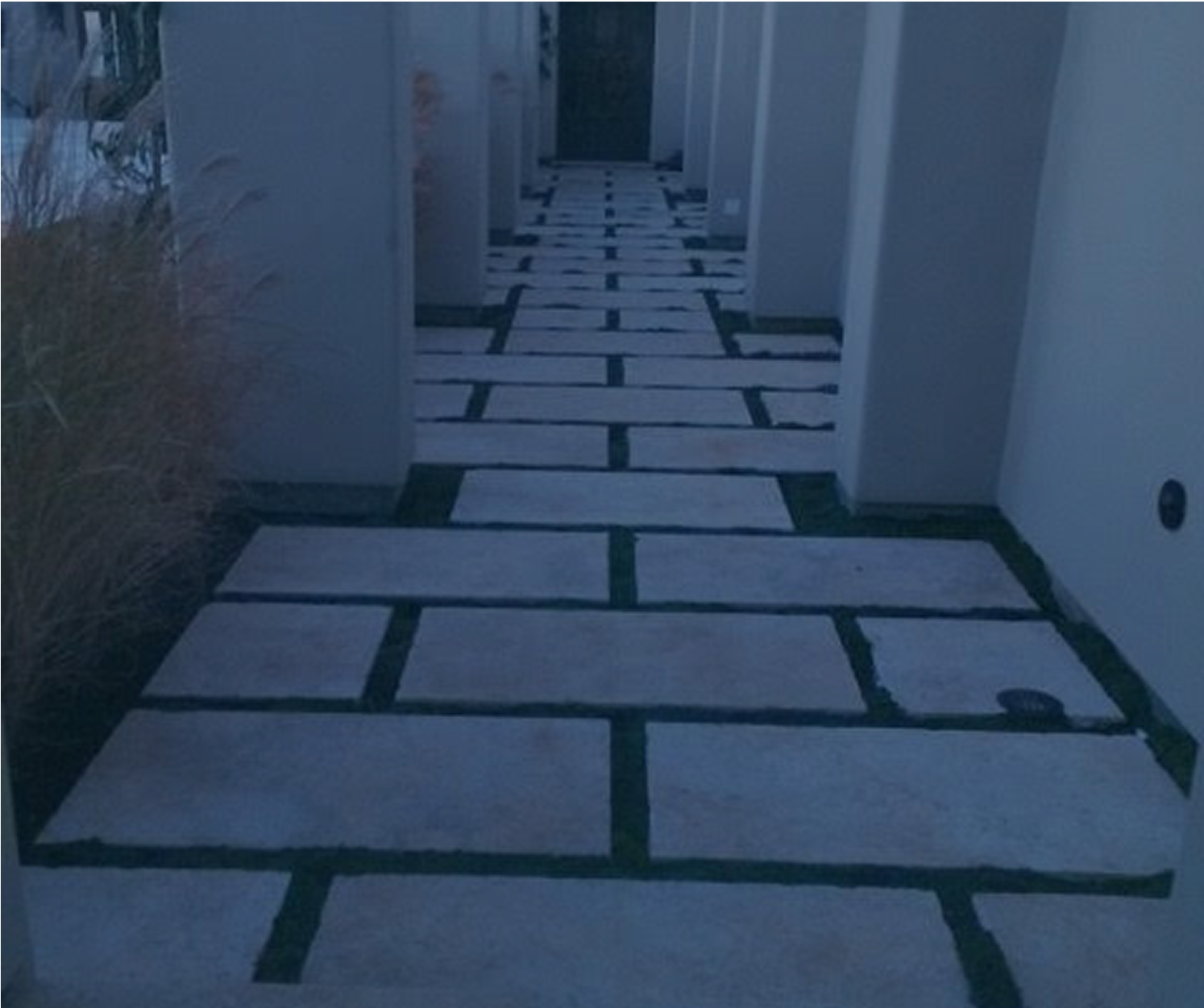 Stone path with dark gaps leading to a doorway, flanked by white pillars, outdoors.