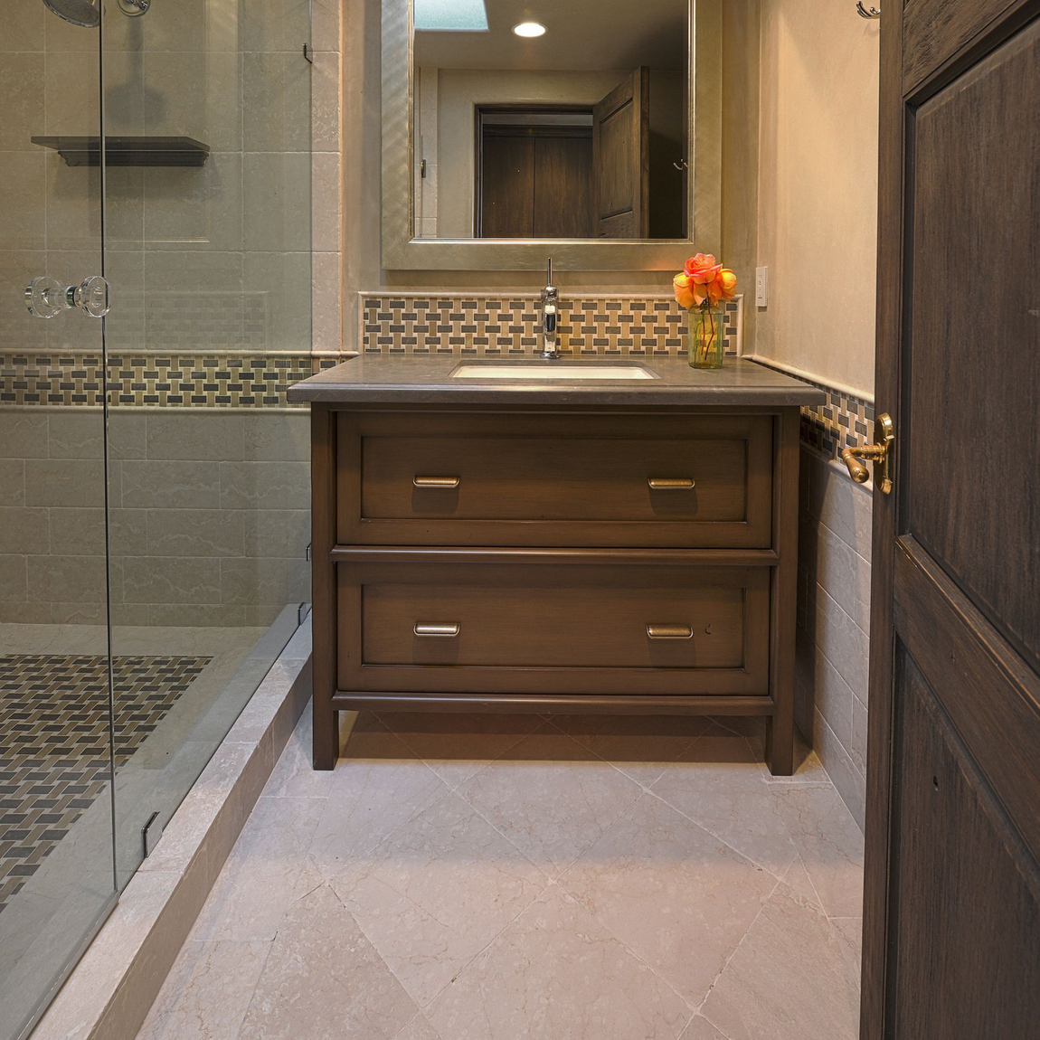 Bathroom with wooden vanity, glass shower, and gray tile.
