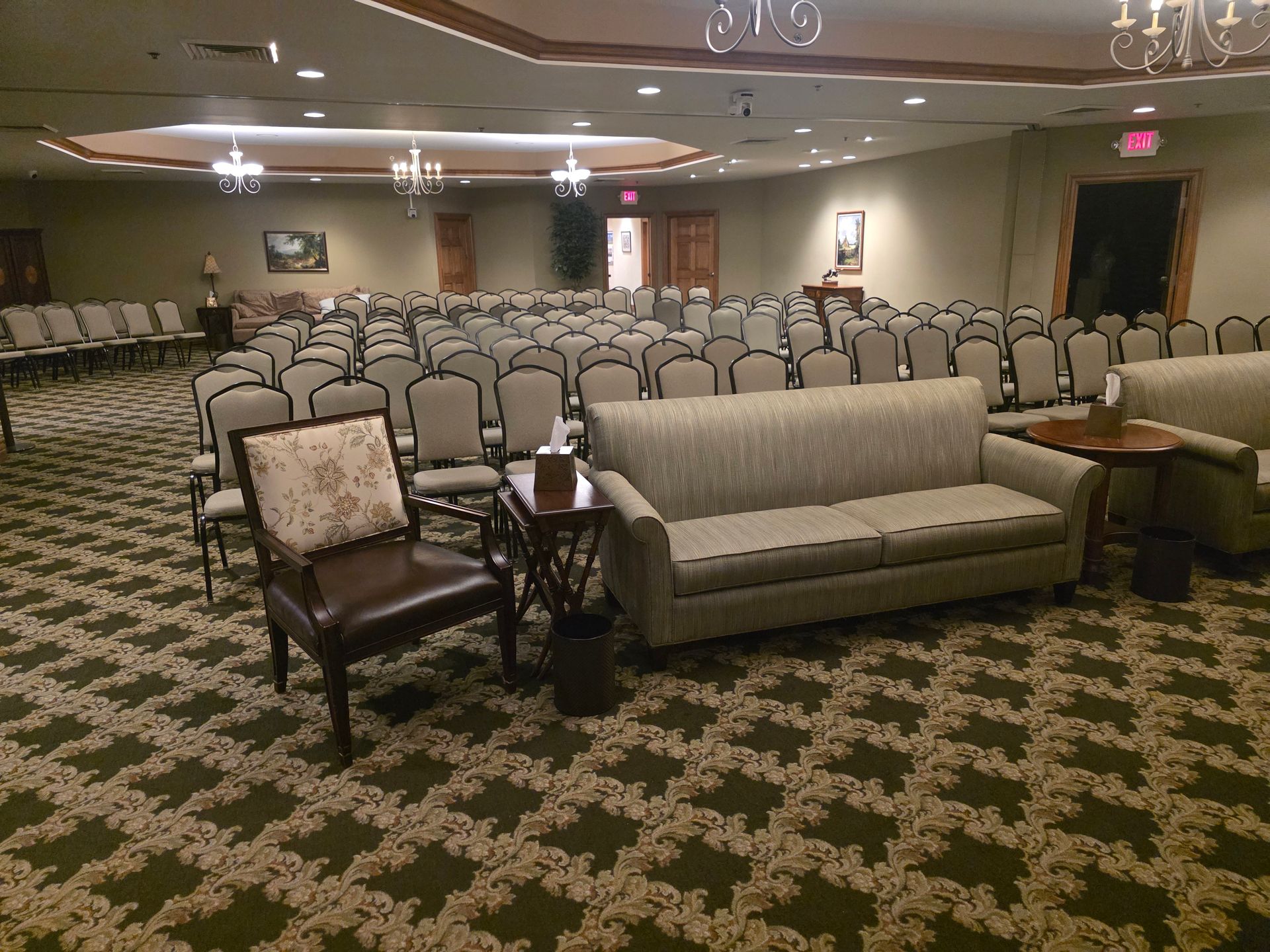 Empty conference room with rows of chairs, a patterned carpet, and a sofa and armchair in front.