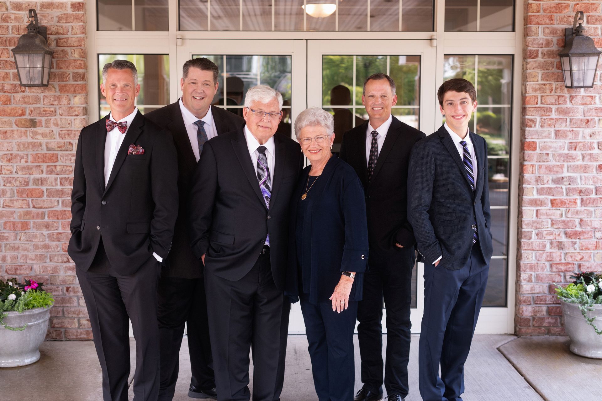 Five people in dark suits posing in front of a brick building entrance