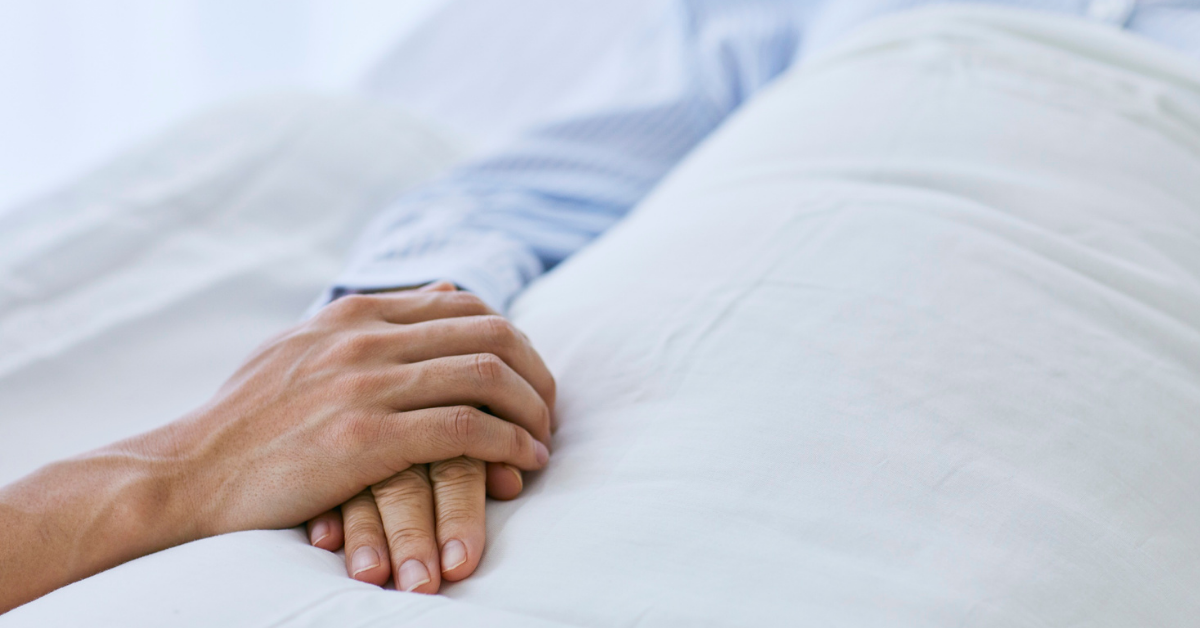 Two hands clasped together on a white bed sheet