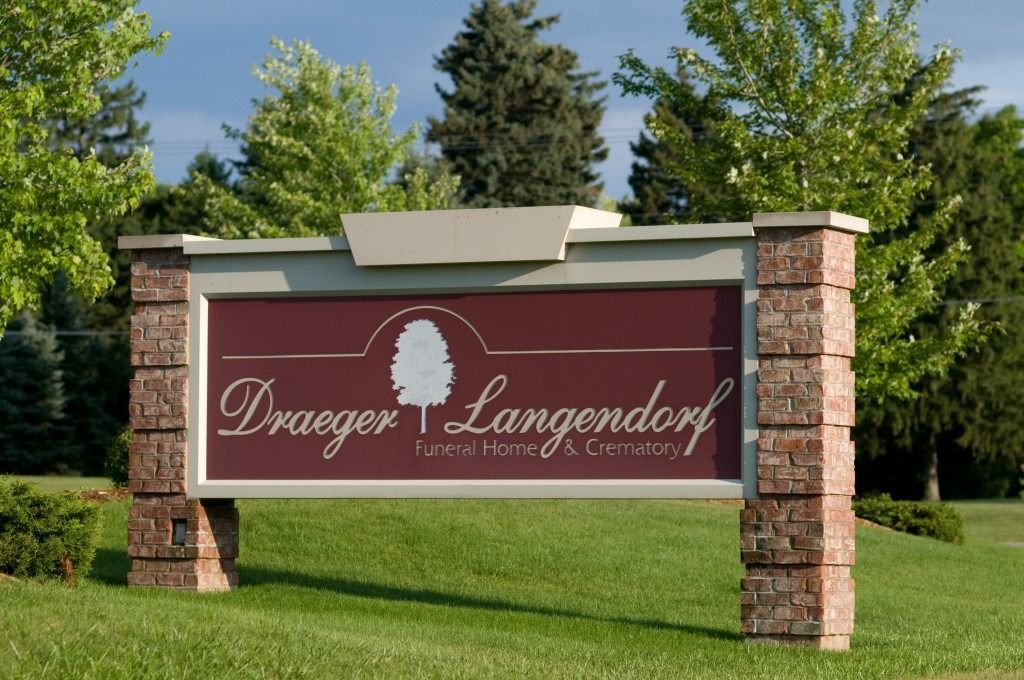 Stone entrance sign reading “Dreyer & Langendorf Funeral Home” on a grassy lawn with trees behind it