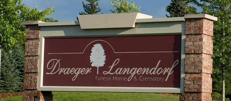 Maroon sign for Droege & Langendorf Funeral Home & Crematory on brick pillars outdoors