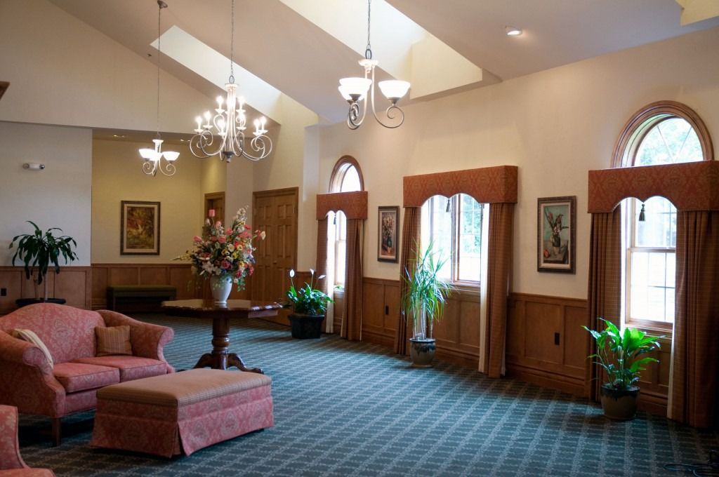 Elegant lobby with pink sofas, chandelier, arched windows, and potted plants.