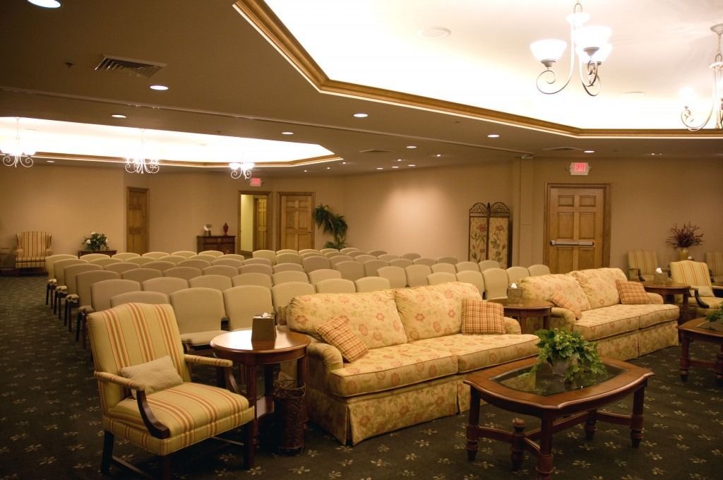 Empty banquet hall with rows of beige chairs, floral sofas, and tables under warm ceiling lights
