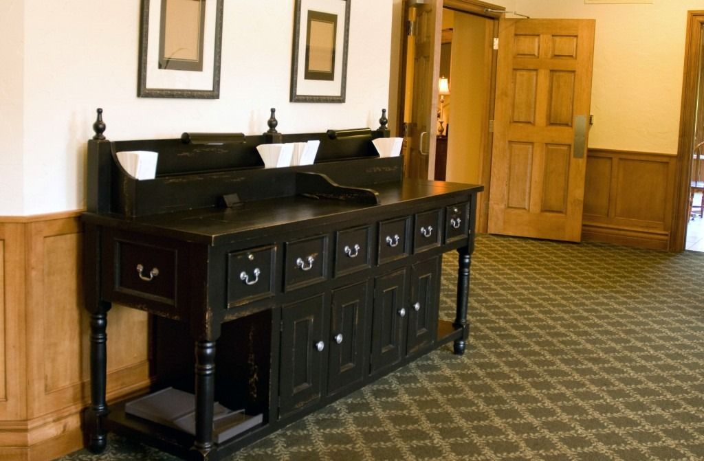 Wooden sideboard with sinks in a patterned hallway, beside an open door and wood-paneled walls