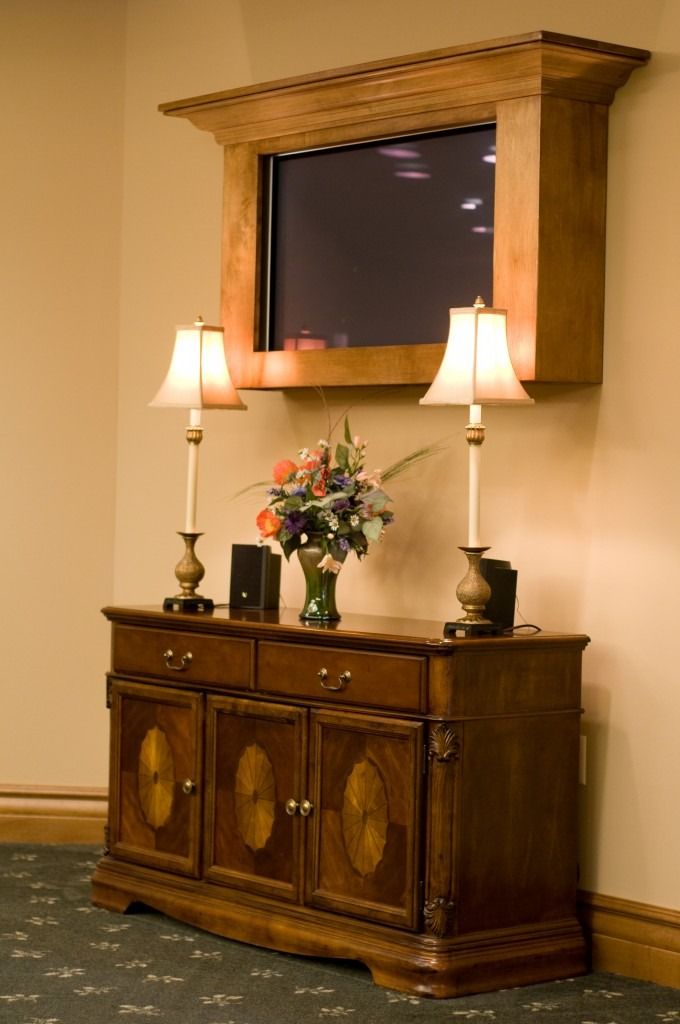 Wooden console table with lamps and flowers beneath a wall-mounted TV in a hallway