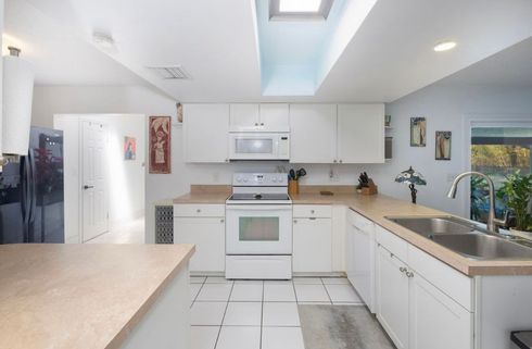 Bright white kitchen with tiled floor, center island, sink, stove, and sunlight from a skylight.