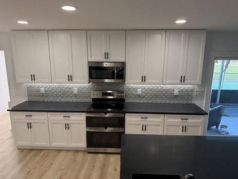 Modern kitchen with white cabinets, dark countertops, stainless steel appliances, and mosaic backsplash.