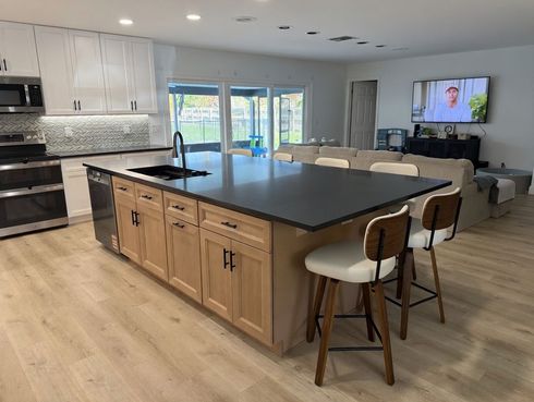 Modern open kitchen and living room with large island, bar stools, and sliding glass doors.