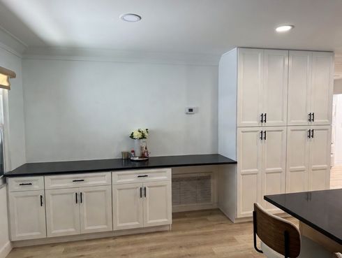 Bright kitchen with white cabinets, dark countertops, and a built-in cabinet wall against light gray walls.