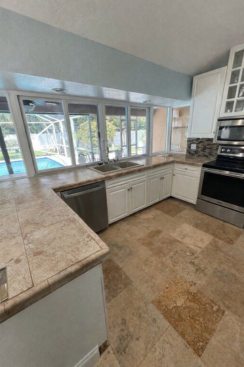 Bright kitchen with granite counters, white cabinets, tile floor, and large windows overlooking greenery
