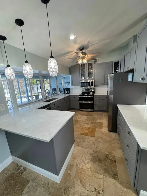 Modern kitchen with gray cabinets, marble counters, pendant lights, and stainless steel appliances