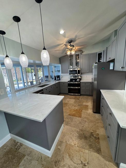 Modern kitchen with gray cabinets, marble counters, pendant lights, and stainless steel appliances