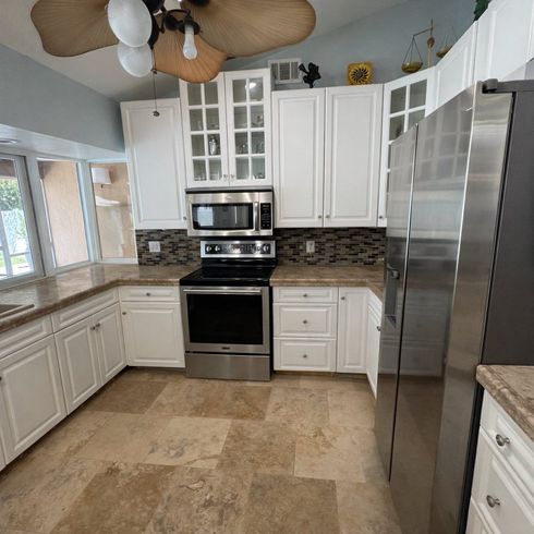 Bright white kitchen with stainless steel appliances, tiled backsplash, and large window.