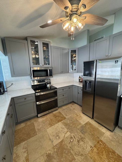 Small kitchen with gray cabinets, black appliances, stainless fridge, and ceiling fan over tiled floor