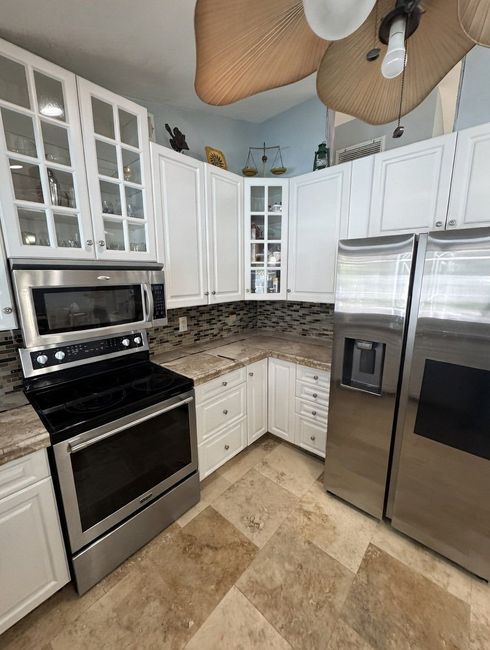 Bright kitchen with white cabinets, stainless steel appliances, and a granite countertop corner.